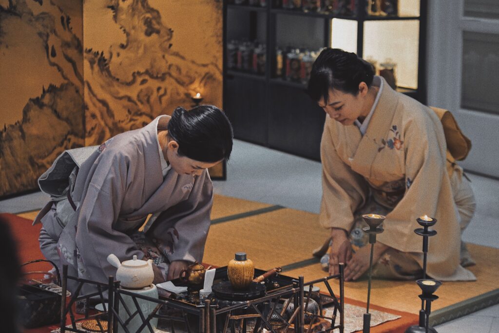 Two women in traditional kimonos performing a Japanese tea ceremony indoors.